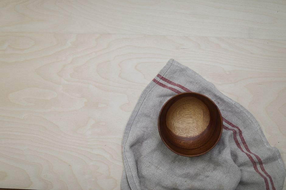A simple wooden bowl placed on a striped linen napkin on a wooden surface, top view.