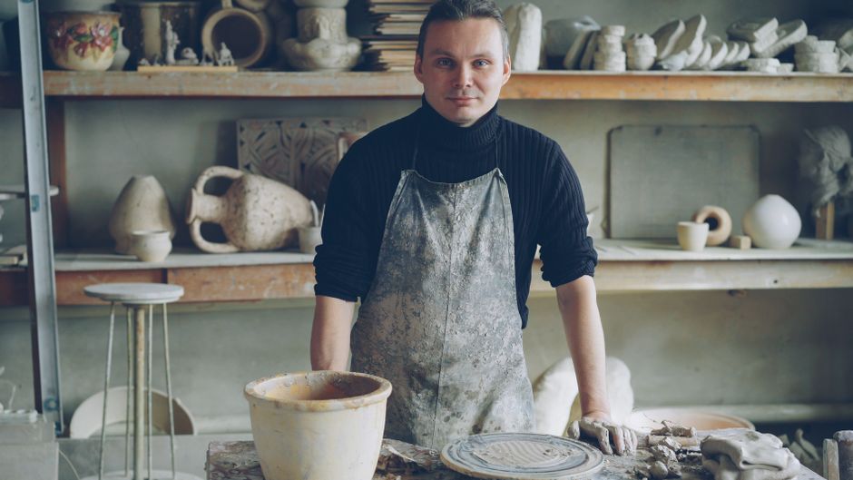 Craftsman in a potter's studio surrounded by handmade ceramics.
