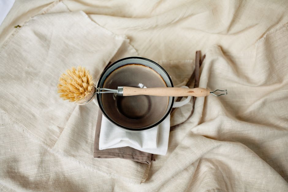 Eco-friendly wooden brush and ceramic bowl on linen fabric for a rustic kitchen vibe.